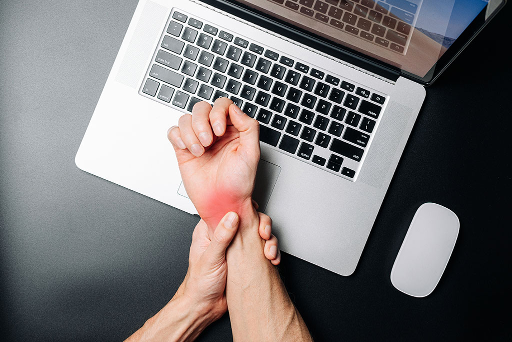 Man Holding His Wrist In Pain Above His Laptop Ultrasound Guided Carpal Tunnel Release